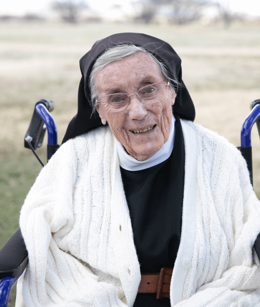 An elderly nun in a wheelchair sitting outside of her monastery