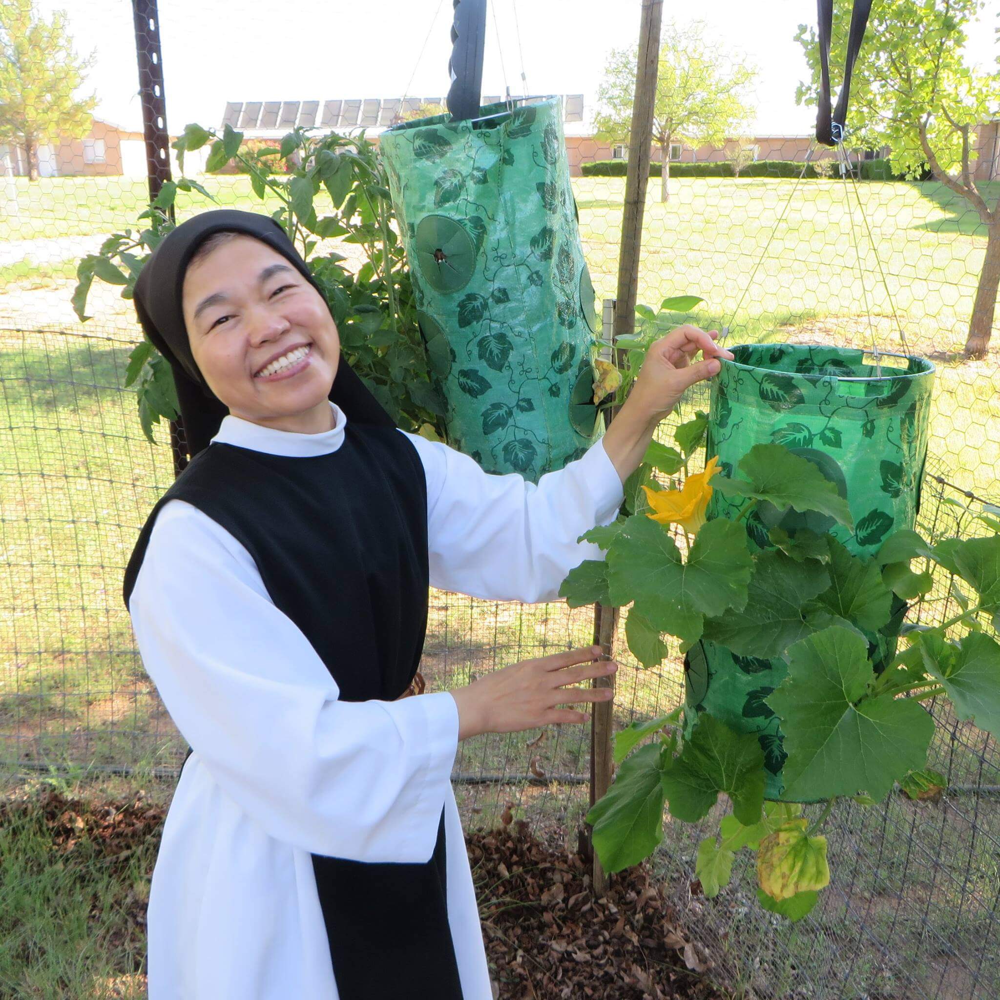 A smiling nun is holding a hanging planter box
